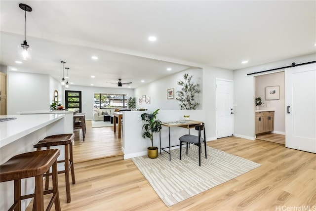 kitchen with decorative light fixtures, a barn door, ceiling fan, and light hardwood / wood-style flooring