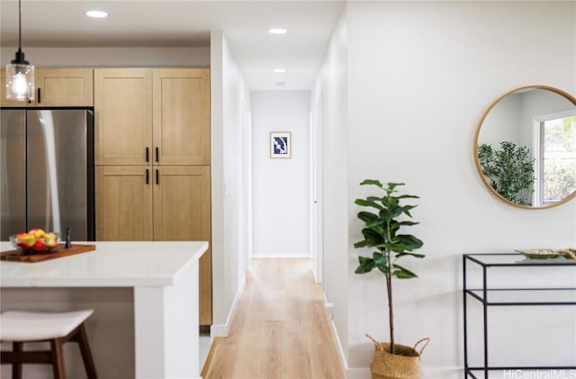 kitchen featuring light brown cabinetry, light hardwood / wood-style flooring, stainless steel refrigerator, and a kitchen breakfast bar