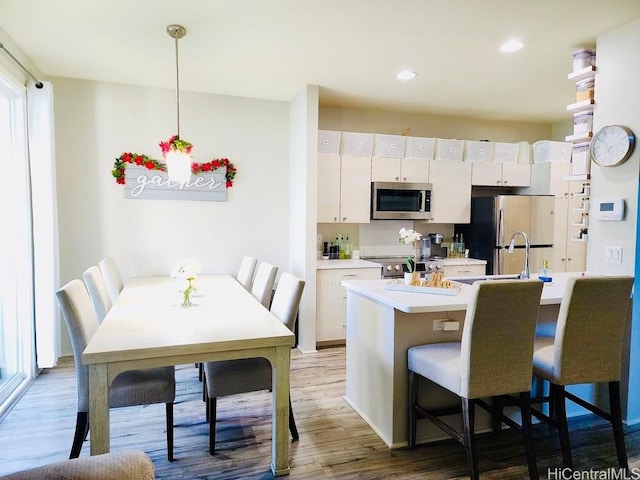 kitchen with appliances with stainless steel finishes, a kitchen breakfast bar, decorative light fixtures, dark hardwood / wood-style floors, and white cabinetry