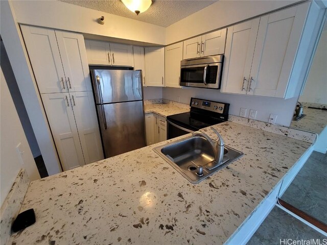 kitchen featuring sink, a textured ceiling, appliances with stainless steel finishes, white cabinetry, and kitchen peninsula