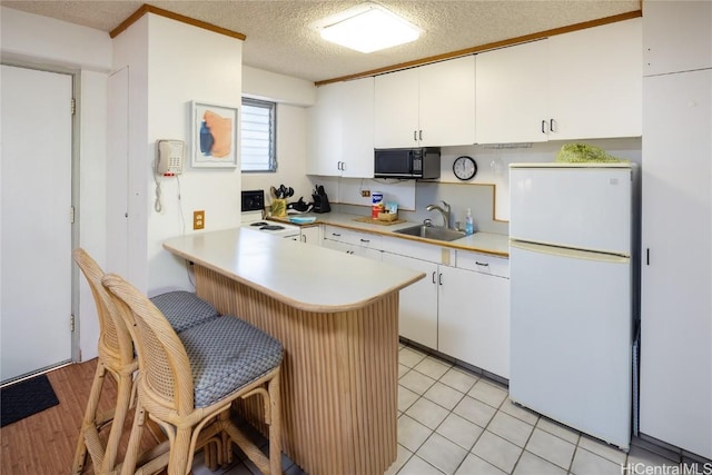 kitchen featuring kitchen peninsula, a textured ceiling, white appliances, sink, and white cabinetry