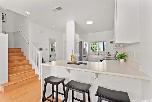 kitchen with kitchen peninsula, stainless steel appliances, light hardwood / wood-style flooring, and white cabinets