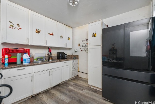 kitchen with white cabinets, black fridge, sink, and hardwood / wood-style flooring