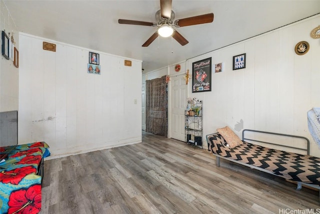 living area with hardwood / wood-style floors, ceiling fan, and wood walls