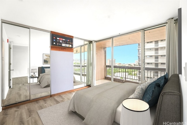 bedroom with access to exterior, light hardwood / wood-style flooring, and a wall of windows