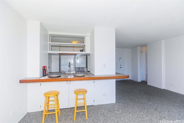 kitchen featuring dark colored carpet, sink, a textured ceiling, kitchen peninsula, and a breakfast bar area