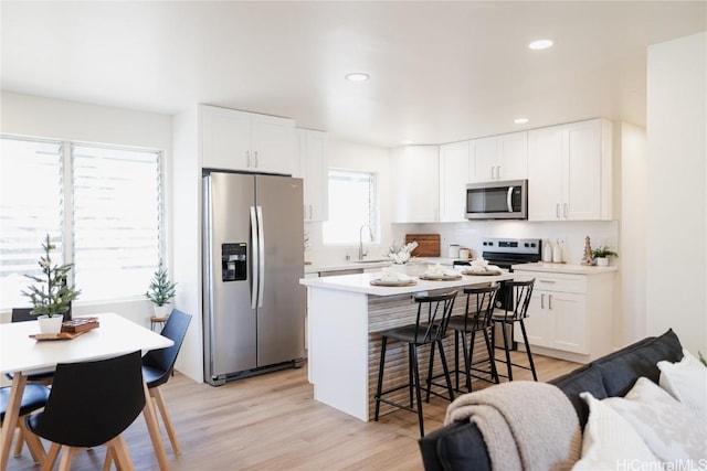 kitchen featuring white cabinets, sink, light wood-type flooring, appliances with stainless steel finishes, and a breakfast bar area