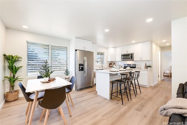 kitchen with a kitchen breakfast bar, light hardwood / wood-style flooring, appliances with stainless steel finishes, a kitchen island, and white cabinetry