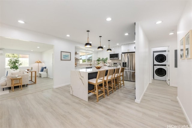 kitchen with decorative light fixtures, appliances with stainless steel finishes, stacked washing maching and dryer, and plenty of natural light