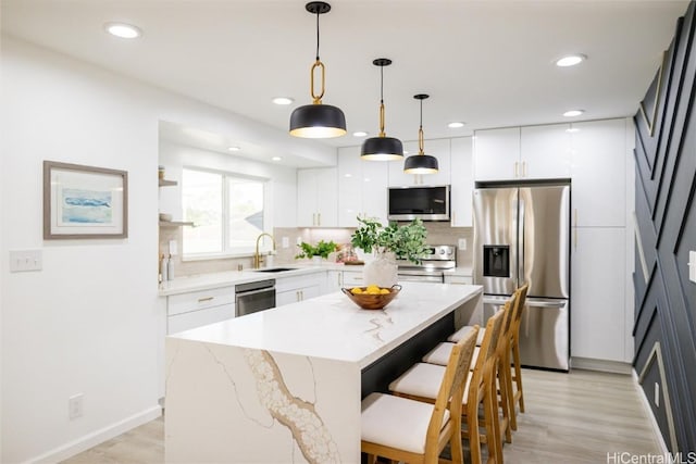 kitchen featuring appliances with stainless steel finishes, decorative light fixtures, a center island, light hardwood / wood-style floors, and white cabinetry