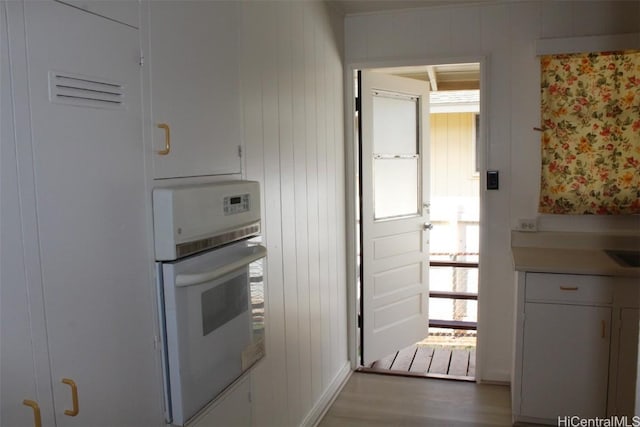 kitchen with white cabinets, hardwood / wood-style flooring, oven, and wood walls