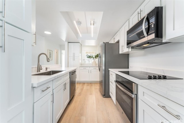 kitchen with light stone counters, stainless steel appliances, sink, light hardwood / wood-style floors, and white cabinetry