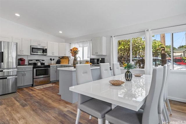 kitchen with appliances with stainless steel finishes, vaulted ceiling, a kitchen island with sink, dark wood-type flooring, and white cabinetry