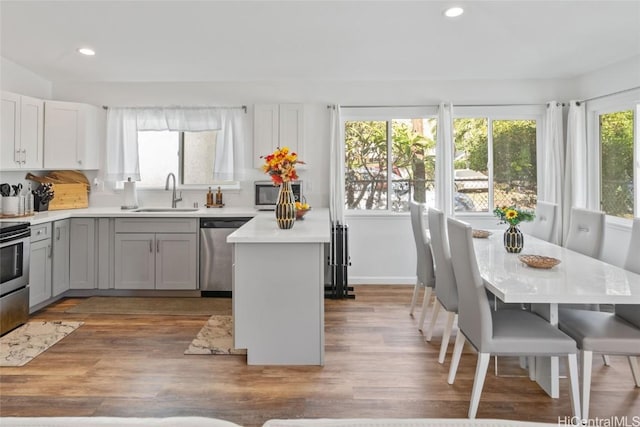 kitchen with stainless steel appliances, sink, hardwood / wood-style flooring, a center island, and gray cabinets