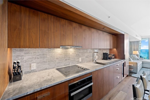 kitchen featuring light stone countertops, sink, stainless steel oven, tasteful backsplash, and black electric stovetop