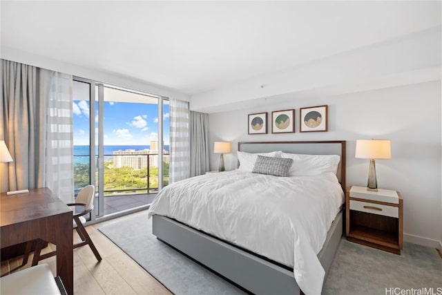 bedroom featuring access to exterior, light wood-type flooring, a water view, and expansive windows