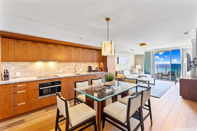 kitchen with decorative backsplash, light hardwood / wood-style flooring, oven, and decorative light fixtures