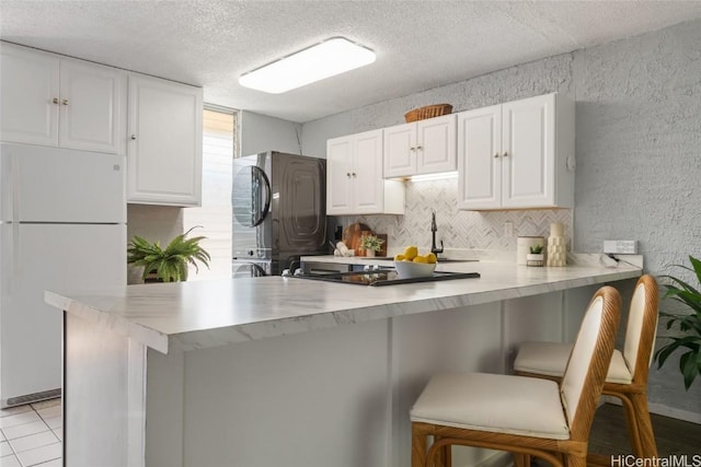 kitchen featuring a breakfast bar, white cabinetry, white refrigerator, kitchen peninsula, and black refrigerator