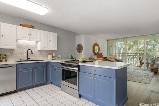 kitchen featuring kitchen peninsula, stainless steel appliances, sink, blue cabinetry, and white cabinets