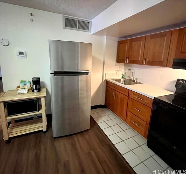 kitchen with stainless steel fridge, light wood-type flooring, ventilation hood, sink, and black / electric stove