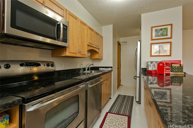 kitchen featuring a textured ceiling, stainless steel appliances, dark stone countertops, and sink