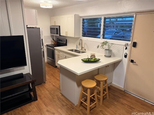 kitchen featuring a kitchen breakfast bar, sink, kitchen peninsula, white cabinetry, and stainless steel appliances