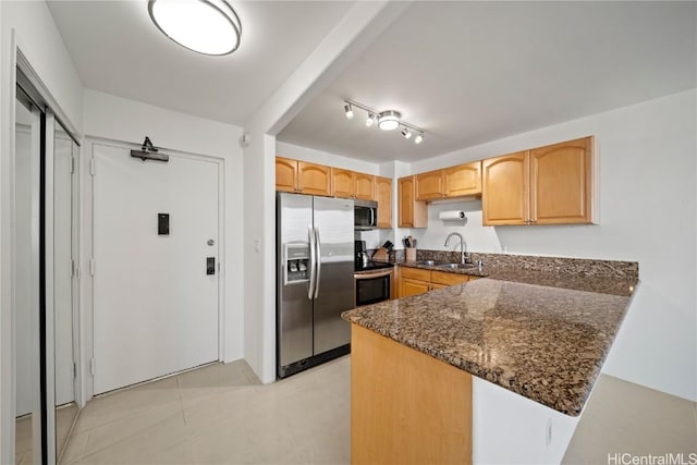 kitchen with dark stone counters, sink, light tile patterned floors, appliances with stainless steel finishes, and kitchen peninsula