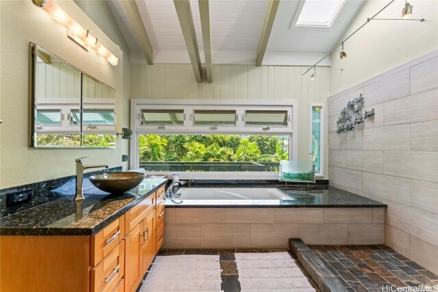 bathroom featuring vanity, beam ceiling, a skylight, and tiled bath