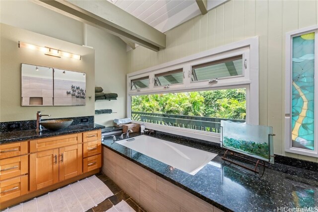 bathroom featuring vanity, beam ceiling, and tiled tub