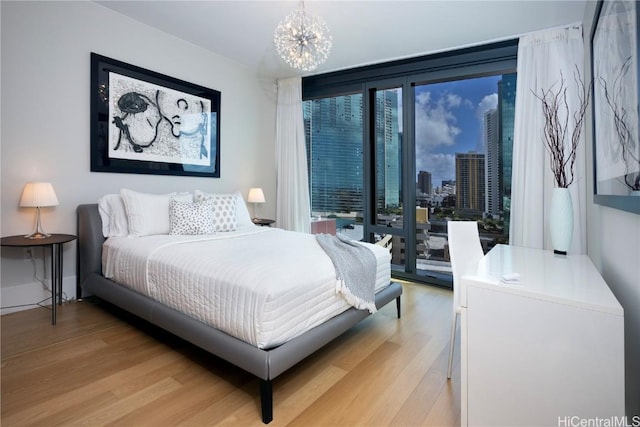 bedroom featuring baseboards, light wood-style flooring, access to outside, a city view, and a notable chandelier