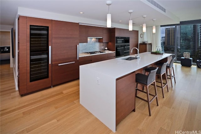 kitchen featuring sink, a kitchen breakfast bar, an island with sink, pendant lighting, and light wood-type flooring