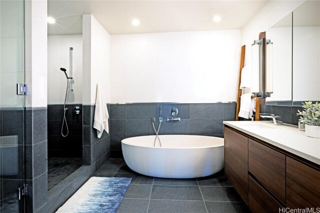 bathroom with tile patterned flooring, vanity, independent shower and bath, and tile walls