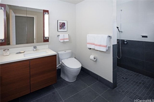 bathroom with tile patterned flooring, toilet, vanity, baseboards, and tiled shower