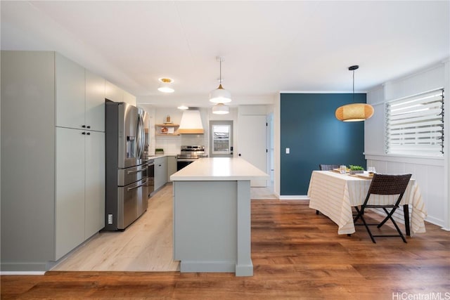 kitchen with hanging light fixtures, stainless steel appliances, light hardwood / wood-style flooring, premium range hood, and a kitchen island