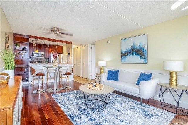 living room featuring ceiling fan, light wood-type flooring, and a textured ceiling