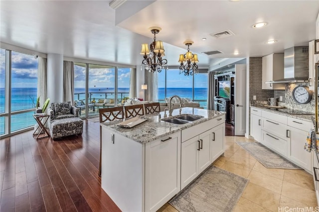 kitchen with a wealth of natural light, sink, a kitchen island with sink, and wall chimney range hood