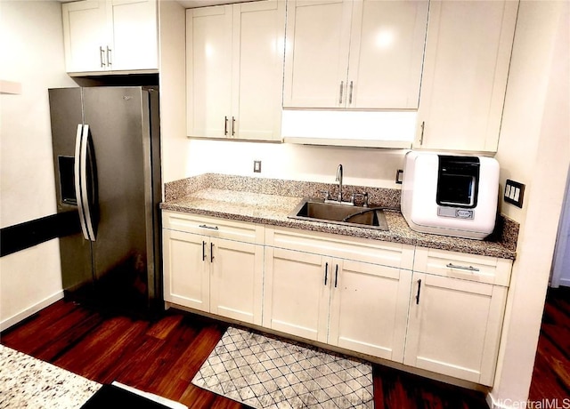 kitchen featuring dark wood-type flooring, light stone countertops, stainless steel refrigerator with ice dispenser, white cabinetry, and a sink