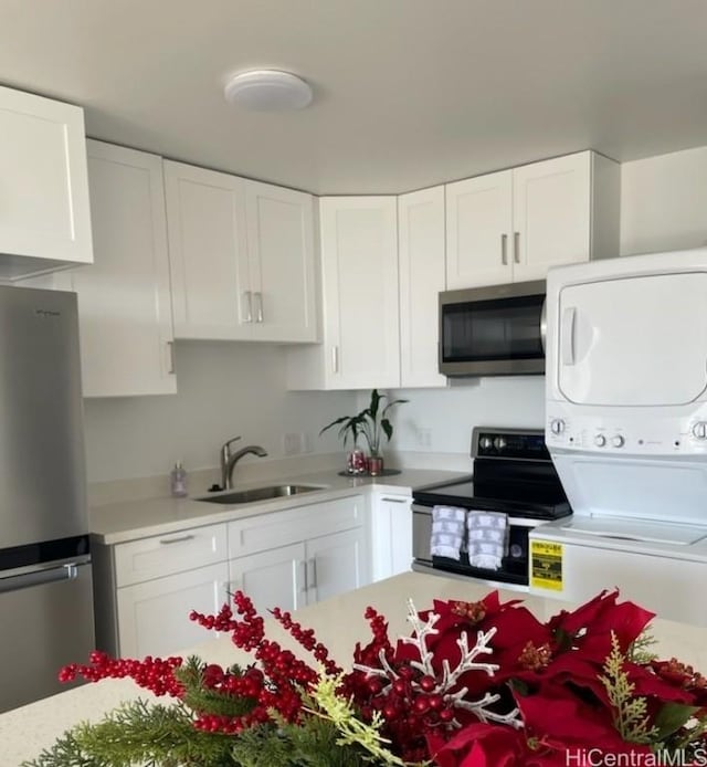 kitchen with white cabinets, sink, stacked washing maching and dryer, and stainless steel appliances