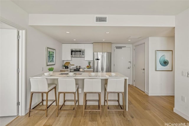 kitchen with a kitchen bar, light wood-type flooring, white cabinetry, and stainless steel appliances