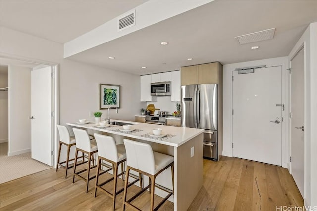 kitchen with a breakfast bar area, sink, stainless steel appliances, and light wood-type flooring