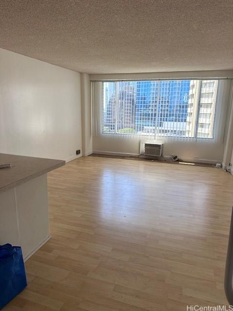 unfurnished living room featuring a textured ceiling, light hardwood / wood-style floors, an AC wall unit, and plenty of natural light