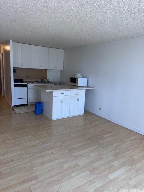 kitchen with a textured ceiling, white cabinets, white appliances, and light wood-type flooring