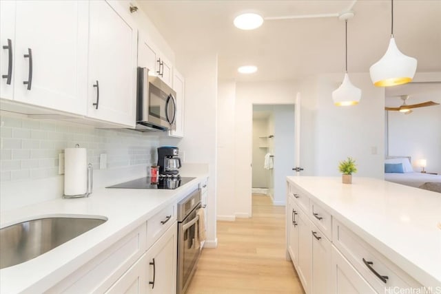 kitchen with appliances with stainless steel finishes, pendant lighting, decorative backsplash, white cabinets, and light wood-type flooring