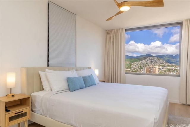 bedroom with a mountain view, wood-type flooring, and ceiling fan