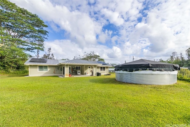 rear view of house featuring solar panels, a patio area, a yard, and a covered pool