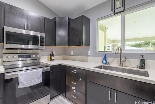 kitchen featuring dark brown cabinets, sink, stainless steel appliances, and vaulted ceiling