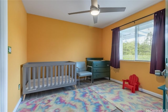 bedroom with ceiling fan, a nursery area, and dark hardwood / wood-style floors