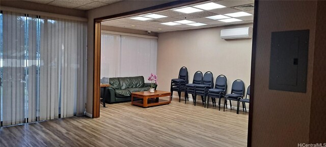 interior space with an AC wall unit, electric panel, a drop ceiling, and hardwood / wood-style flooring