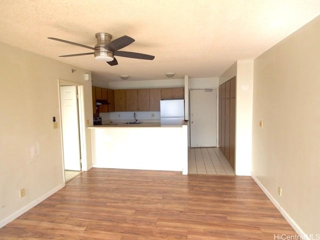 kitchen featuring white refrigerator, sink, light hardwood / wood-style flooring, ceiling fan, and a textured ceiling