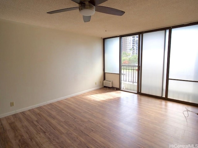 spare room featuring ceiling fan, light hardwood / wood-style flooring, expansive windows, a wall mounted AC, and a textured ceiling